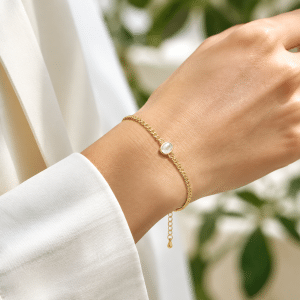 Bracelet souple plaqué or pendentif ovale blanc porté par une femme
